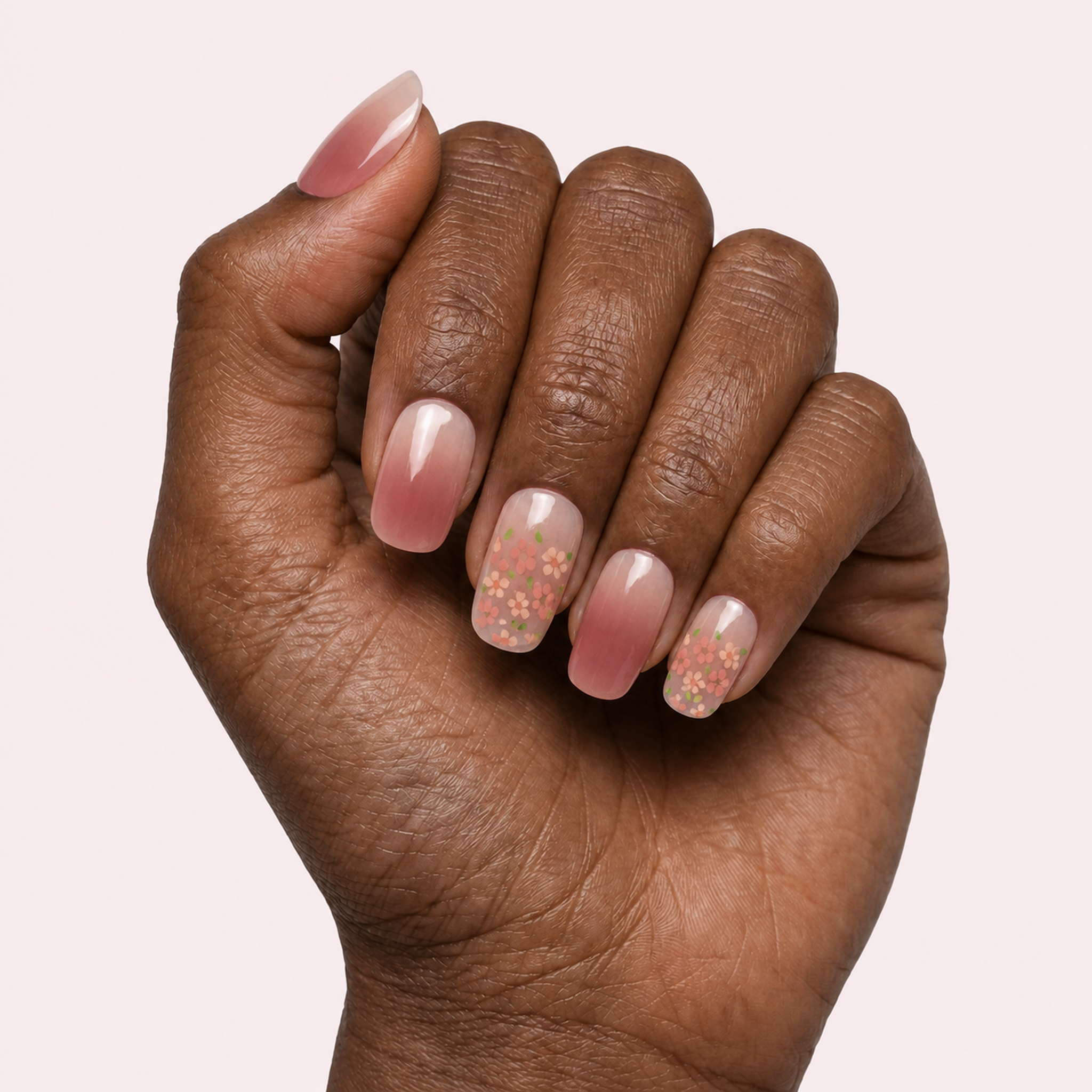 Pink nude gel nail strips with floral blossom accents worn on a deep skin tone hand