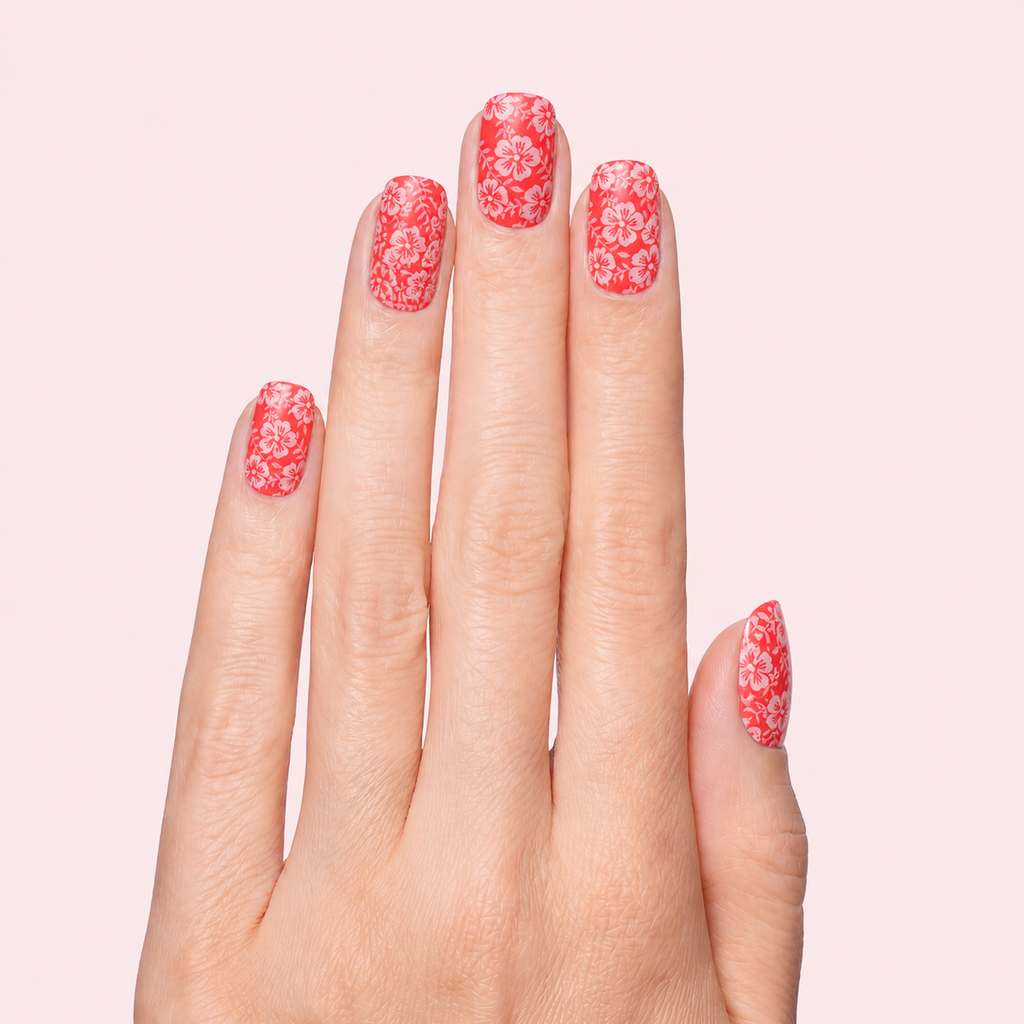 Coral red gel nail strips with white hibiscus flower print worn on a light skin tone hand