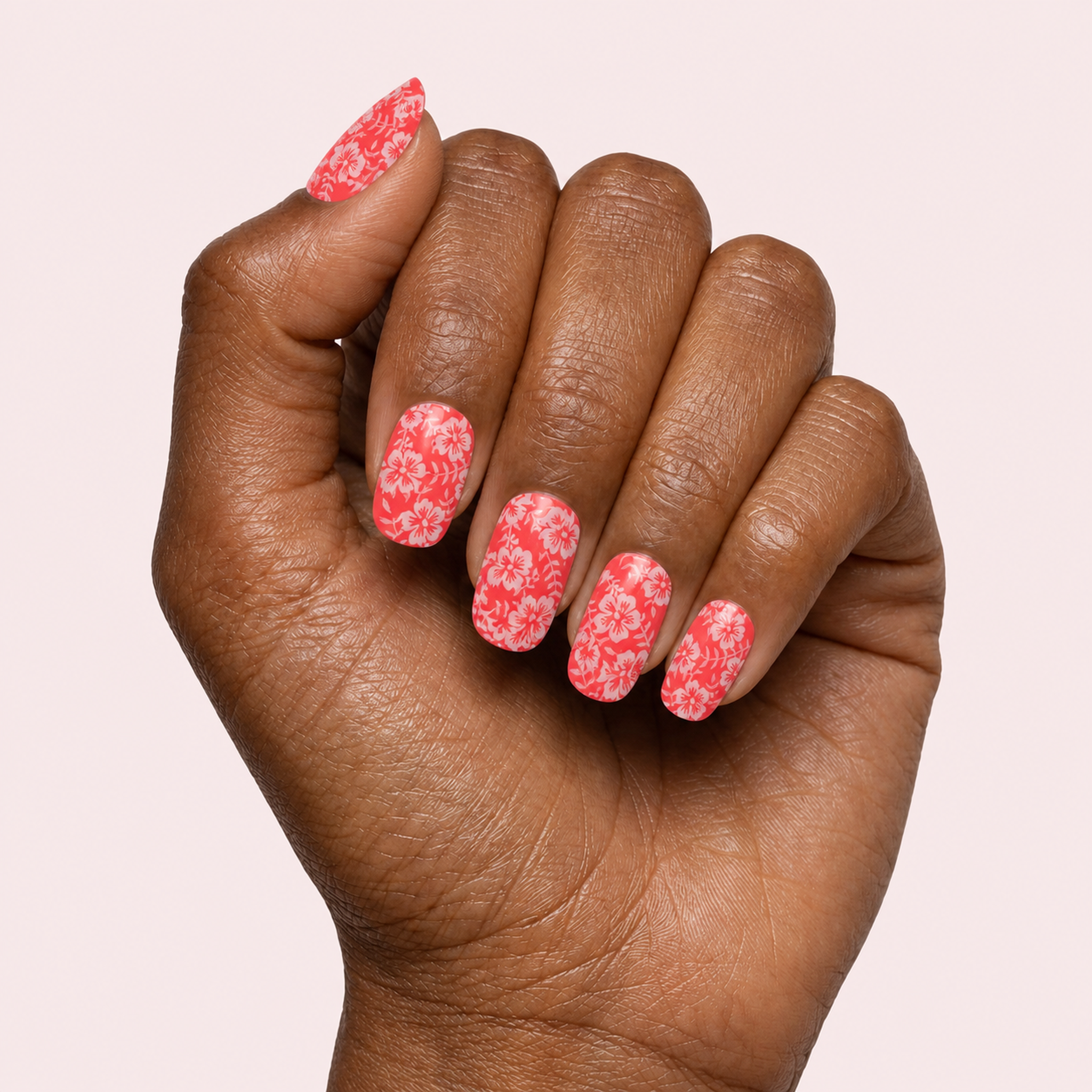 Coral red gel nail strips with white hibiscus flower print worn on a deep skin tone hand